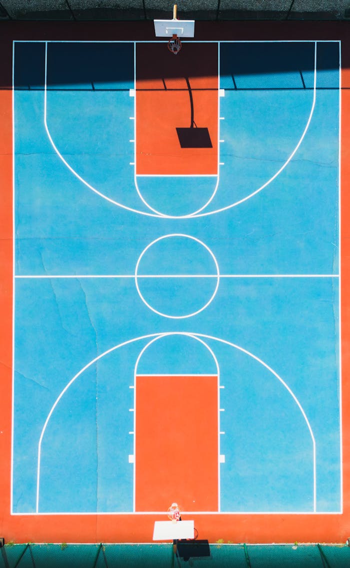 services-02 Top-down view of a vibrant blue and red basketball court with clear lines and two hoops.
