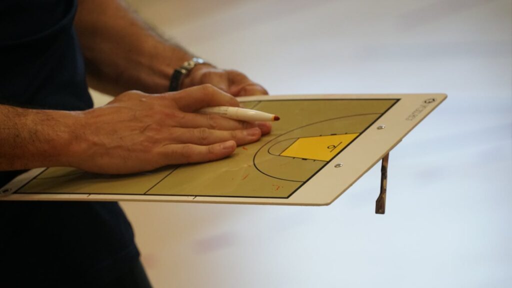 pexels photo 32688082 Close-up of a coach using a basketball tactics board to plan game strategy indoors.