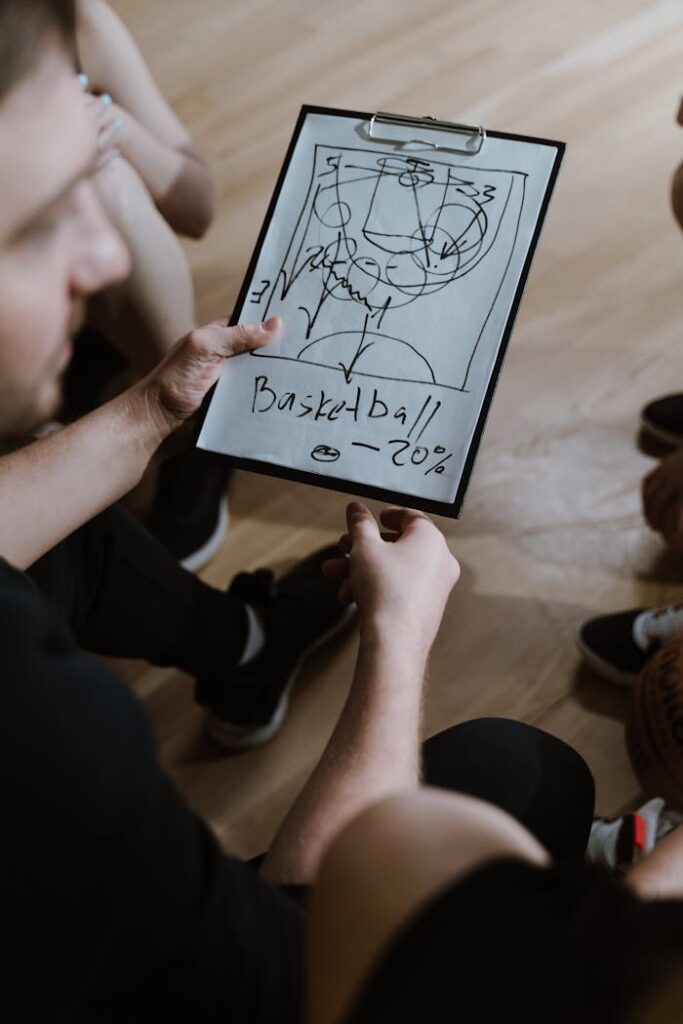 pexels photo 6767042 Coach presents a basketball strategy on clipboard during indoor team huddle.