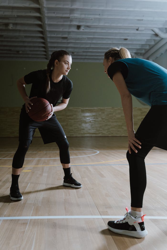 our-services-3 Two female athletes face-off on an indoor basketball court, showcasing competitive spirit.