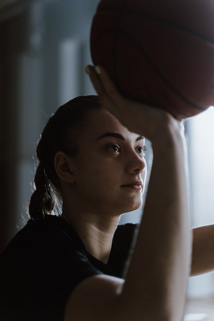 Teen girl focusing on making a basketball shot indoors, showcasing determination and skill.